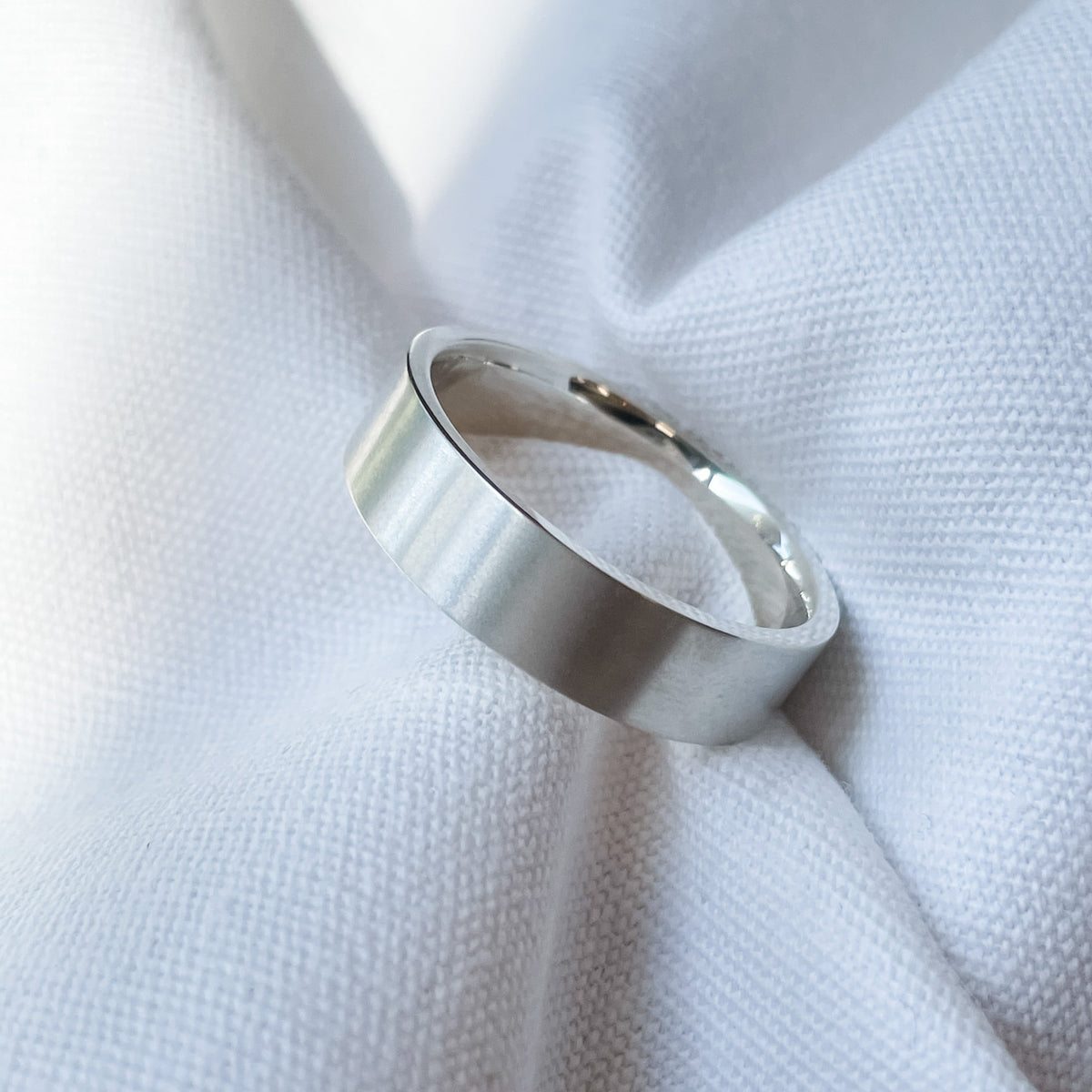 Silver luxury ring on textured white fabric, showcasing its polished finish. Ideal for wedding band or high-end jewellery enthusiasts.
